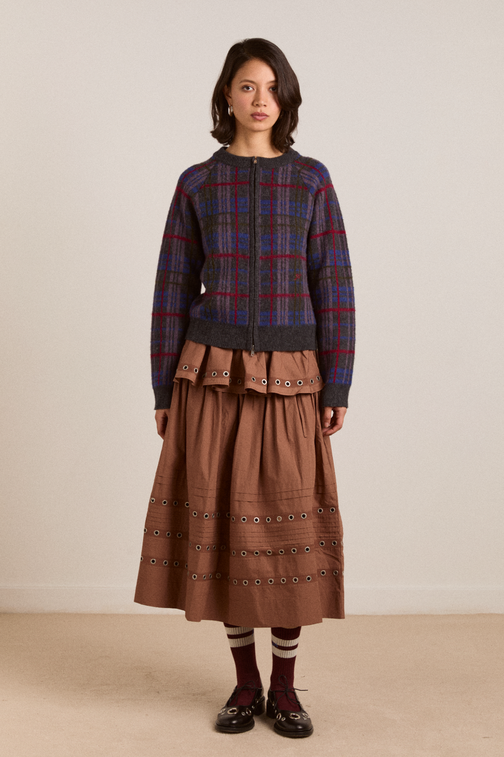 Woman wearing a plaid sweater and brown skirt against a plain background