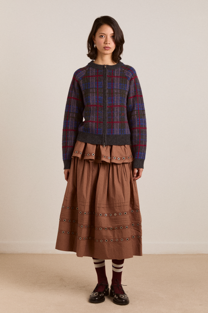 Woman wearing a plaid sweater and brown skirt against a plain background